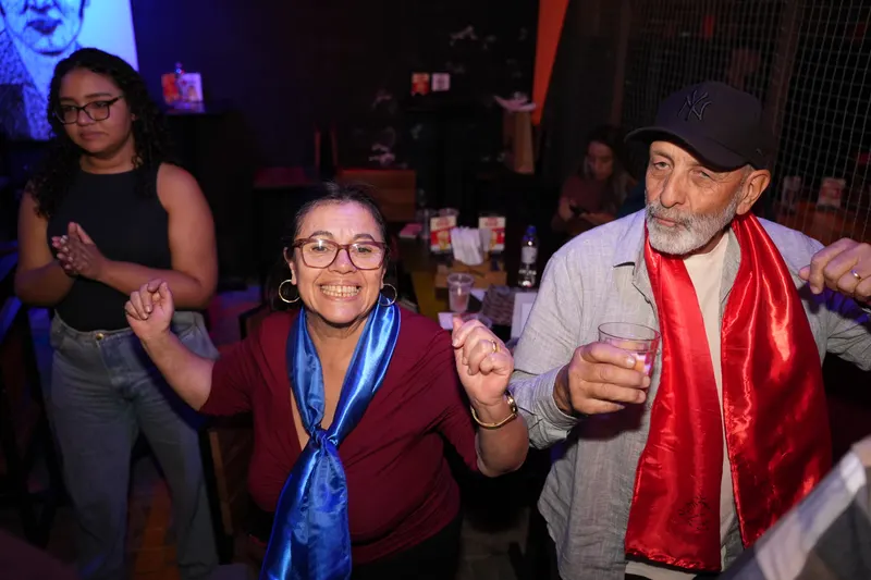 Casal da plateia dançando com lenços de cetim azul e vermelho no pescoço